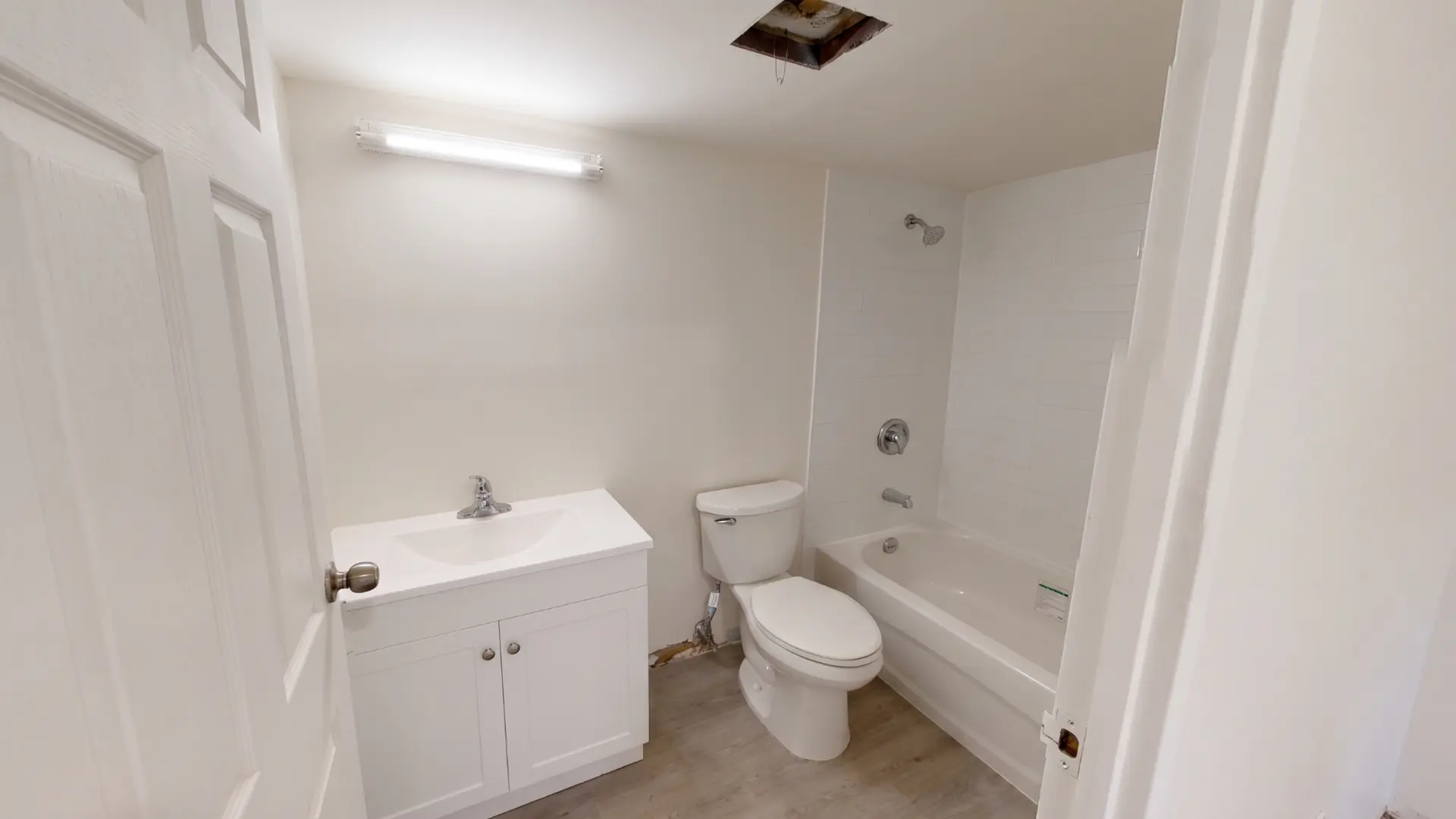 Completed bathroom with white vanity, tiled tub surround and new flooring