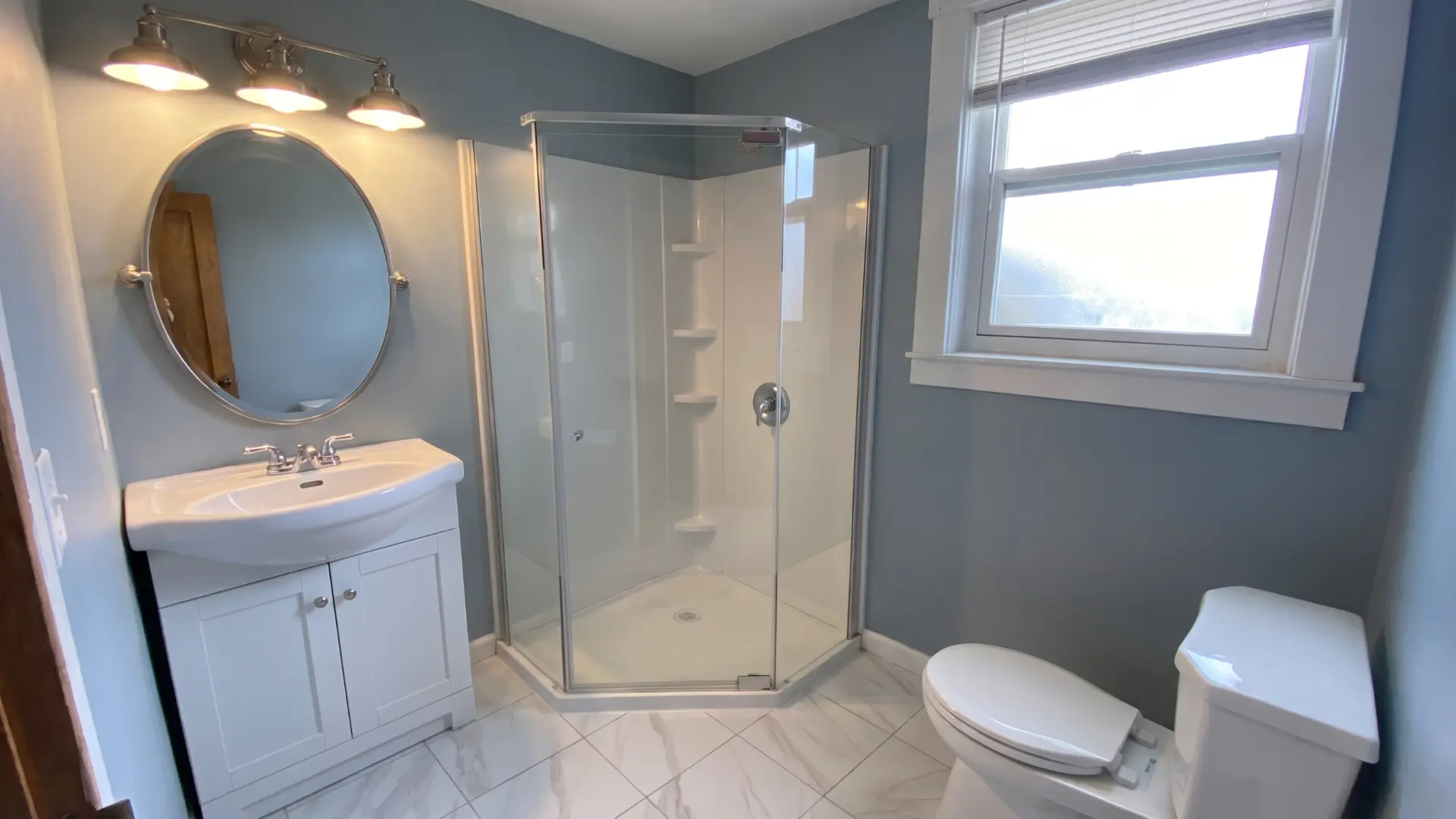 Completed bathroom with neo angle glass shower, white vanity and marble look tile floor