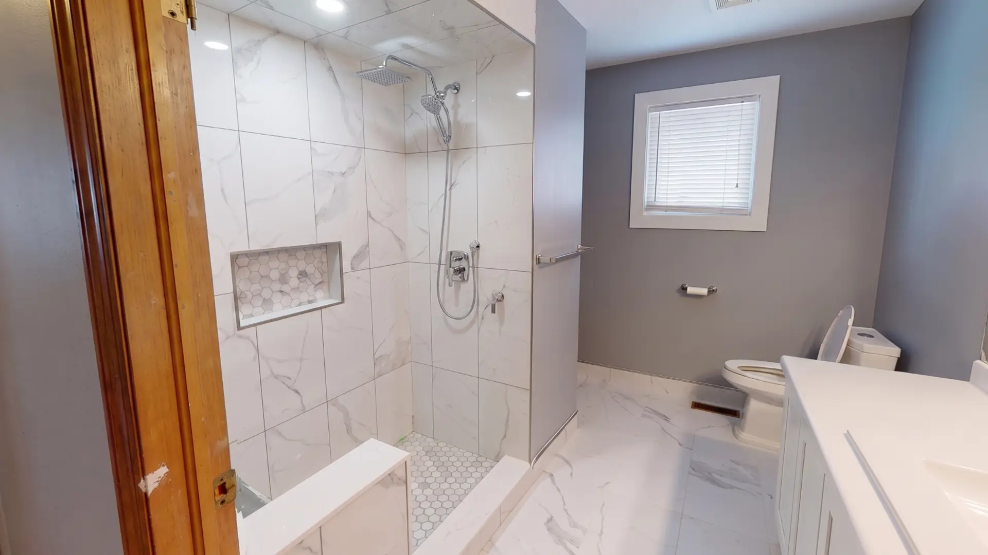 Completed bathroom with a walk-in marble look shower, tiled niche, bench and matching floor tile
